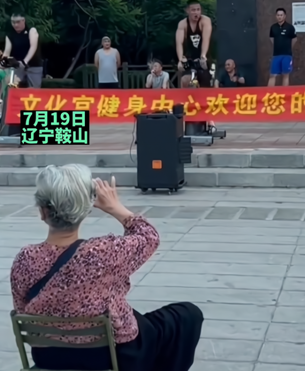 肌肉小伙在广场健身，大妈搬板凳坐对面观看，看不清楚拿手机录像